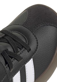 Czarny tenis z teksturowanej skóry i paneli z zamszu, czarne sznurowadła, białe paski po bokach oraz brązowa gumowa podeszwa.