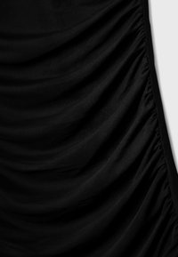 Tissu noir avec un ruché vertical pour la texture, une finition lisse et une coupe ajustée sur le côté gauche. Pas de fermetures visibles.