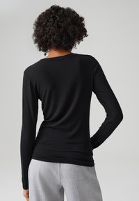 Top nero a maniche lunghe con costine e scollatura rotonda, abbinato a pantaloni grigi chiari. Il tessuto sembra morbido con una leggera texture.
