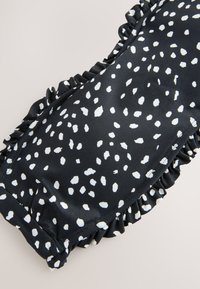 Mustast materjalist valgete täppidega riie, mille servad on kortsuliselt viimistletud. Materjal on sile ja läikiv ning mõnusalt pehme tekstuuriga.