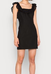 Robe noire avec un décolleté carré et des volants en dentelle sur les épaules. Le tissu est lisse avec une silhouette ajustée.