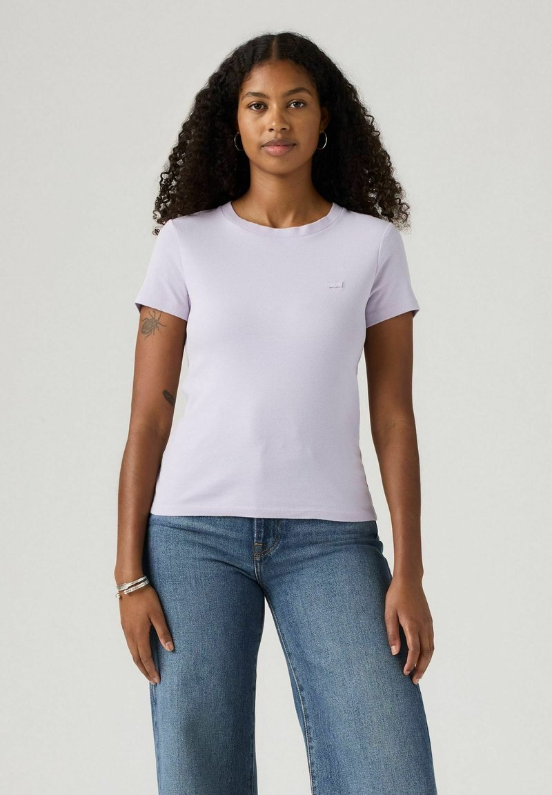 T-shirt in cotone lavanda con maniche corte, scollo rotondo e discreto logo sul davanti. Abbinato a jeans a gamba larga di un blu chiaro.