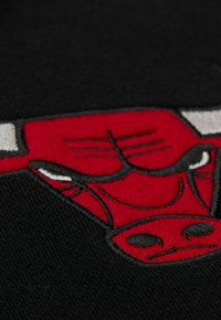 Tessuto nero con un logo di toro rosso ricamato in modo prominente, con accenti neri e bianchi, che mostrano dettagli e textures facciali distintivi.