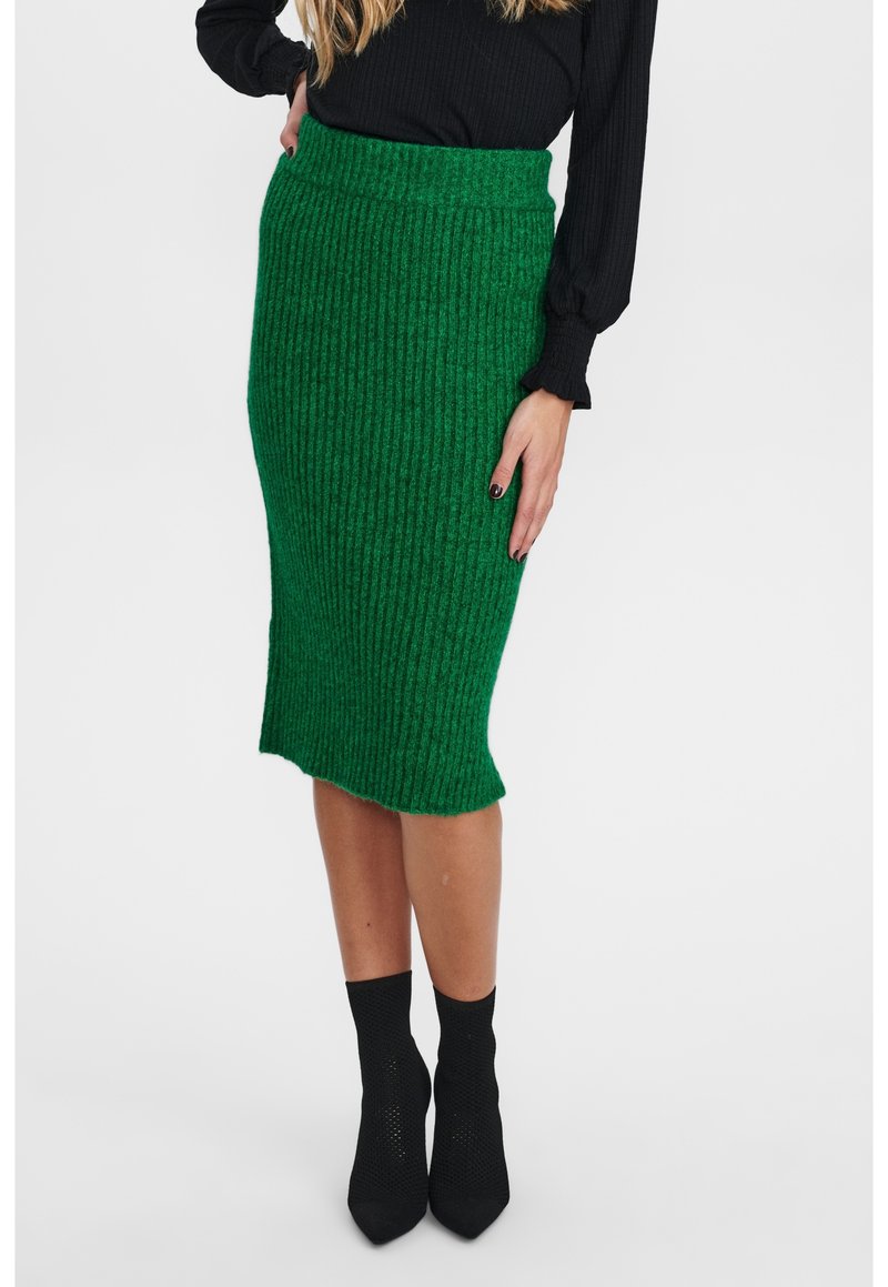 Grün gestreifter Strick-Midirock mit figurbetonter Silhouette, strukturiertem Muster und einem dezenten asymmetrischen Saum, kombiniert mit schwarzen Stiefeletten.