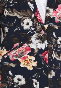 Květinový blazer s tmavě modrým pozadím, velkými barevnými květinami, strukturovaným designem, zapínáním na jeden knoflík a dvěma předními kapsami.