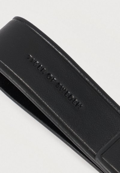 Correia de couro preto com o nome da marca "Tiger of Sweden" gravado em letras maiúsculas.