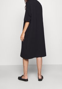 Robe t-shirt noire oversize en coton. Caractéristiques : manches courtes, design simple et longueur au milieu du mollet. Portée avec des sandales noires.