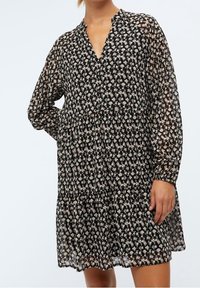 Robe noire à fleurs fabriquée en tissu léger et transparent. Présente un décolleté en V, des manches longues et une jupe à volants avec de petits motifs de fleurs délicates.