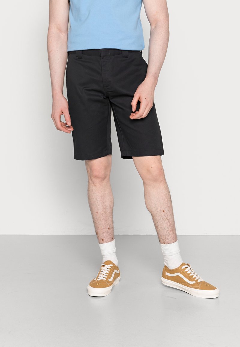 Black shorts with a smooth texture, straight cut, and belt loops, paired with a light blue fitted shirt and tan sneakers.