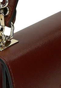 Bruine leren handtas met een gladde textuur. Heeft een rechthoekige vorm, goudkleurige hardware en een kettingaccent op de handgreep.