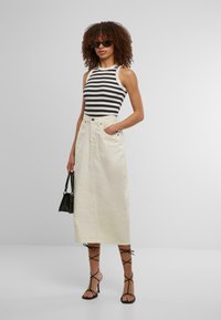 Top a righe bianche e nere senza maniche, abbinato a una gonna di jeans color crema di lunghezza media e sandali neri con cinturini.