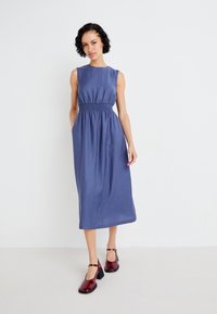 Blue sleeveless dress with gathered waist, knee-length, made of lightweight fabric. Paired with glossy burgundy block-heel shoes.