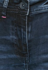 Pantalones vaqueros de denim negro con cierre de botón, detalles de costura sutiles y una textura suave y ligeramente brillante. Incluye un bolsillo frontal.