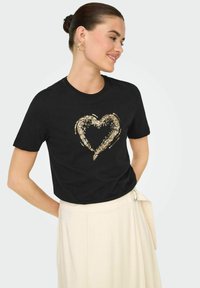 Camiseta de algodón negra con un diseño de corazón lleno de lentejuelas doradas. Tiene un escote redondo y mangas cortas. La tela parece suave.