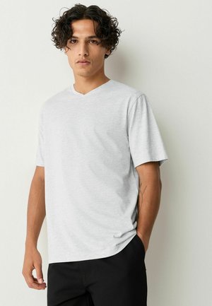 T-shirt gris clair à col en V en tissu doux et texturé. Manches courtes, coupe décontractée, associé à un pantalon noir. Design simple sans embellissements.