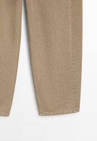 Untere Abschnitt einer beige-farbenen, geraden Jeanshose aus Denim-Stoff vor weißem Hintergrund.