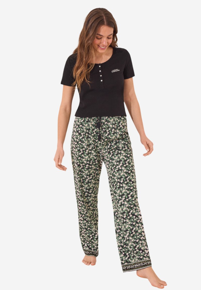 Zwarte top met korte mouwen en knoopsluiting, gecombineerd met groene broek met bloemenpatroon met een koord in de taille en een decoratieve zoom.
