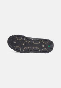 Black rugged sneaker sole with aggressive treading, featuring raised geometric patterns and a green accent detail for traction.