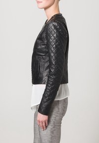 Giacca in pelle trapuntata nera con un design aderente, colletto rotondo, due tasche laterali e sottili accenti lungo le cuciture delle spalle.