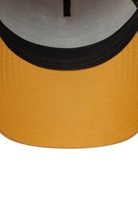 Gorra de visera plana con una parte frontal de tela amarilla y parte inferior negra, presentando una superficie texturizada y acentos cosidos. Interior forrado con tela clara.