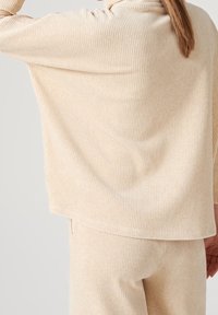 Ensemble de loungewear beige à côtes fabriqué en tissu doux ; comprend un haut ample et drapé et un pantalon ajusté. Détail de la texture visible dans le tissu.