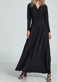 Svart maxiklänning med långa ärmar, crossover V-ringning, samlad midja, flödande kjol och mjuk textur. Kombinerad med sandaler med klack och remmar.