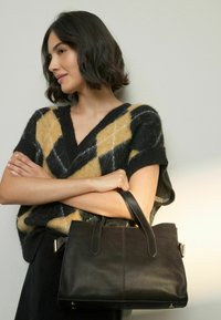 Black leather tote bag with dual handles, smooth texture, and minimal stitching. The bag has a structured shape and is held casually.