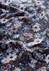 Blått tyg med vita, rosa och bruna blommönster som inkluderar prästkragar och blad, visat med mjuka veck och textur.