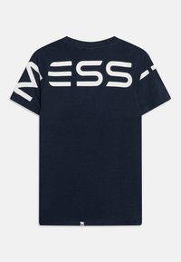 Marineblå t-skjorte med korte ermer som har store hvite "NESS"-bokstaver på ryggen. Laget av mykt stoff, med rund hals og klassisk passform.