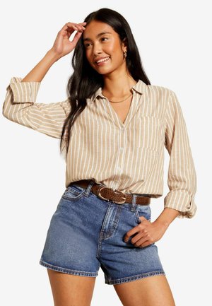 En beige skjorte med hvide lodrette striber, parret med blå denimshorts og et brunt bælte med en rund spænde.