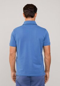 Niebieska bawełniana koszulka polo z krótkimi rękawami, z płaskim kołnierzykiem i gładkim, lekko teksturowanym wykończeniem. Widok z tyłu nie zawiera grafik.