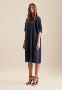 Navyblaues Leinenkleid mit lässigem Schnitt, kurzen Flatterärmeln und knielanger Länge. Getragen mit schwarzen Riemchen-High Heels.