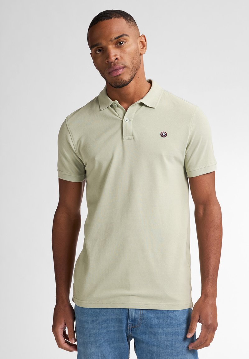 Polo shirt verde chiaro con colletto e maniche corte, caratterizzato da un piccolo logo ricamato rotondo sul lato sinistro. Tessuto a trama semplice.