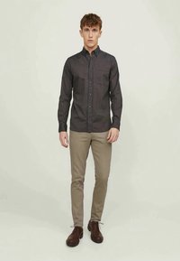 Camisa abotoada em cinza escuro com finas riscas verticais, combinada com calças caqui claras e sapatos castanhos escuros. Textura de tecido suave.
