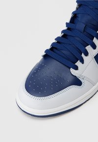 Μπλε και λευκά αθλητικά παπούτσια με γυαλιστερό δέρμα, τρύπες στο μπροστινό μέρος, ναυτικές επίπεδες κορδόνες και καουτσούκ σόλα.