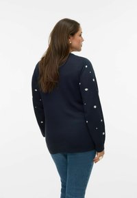 Granatowy sweter wykonany z dzianiny, z okrągłym dekoltem, ozdobiony białymi grochami na rękawach, o luźnym kroju.