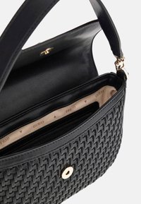 Sac à main en cuir noir tressé avec rabat, fermoir doré, poche intérieure zippée et doublure beige imprimée du logo "GUESS".