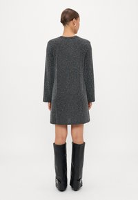 Vestito nero a fantasia multicolore con maniche lunghe, taglio dritto e scollatura rotonda, abbinato a stivali neri al ginocchio.