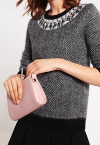 Pull gris en tricot avec un ourlet noir et un col décoratif orné de perles. Tenant une pochette en cuir rose doux.