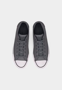 Ζευγάρι σκουρόχρωμων γκρι χαμηλών sneakers Converse All Star με λευκές ρηχτές μύτες και κορδόνια, σε λευκό φόντο, εμφανιζόμενα από πάνω.