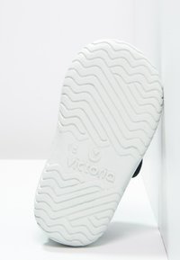 Suela de zapato de goma blanca con un patrón de relieve ondulado y un logo en relieve. El zapato está posicionado sobre un fondo claro.