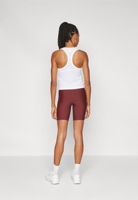 Completo sportivo composto da una canottiera bianca con schiena a conchiglia e pantaloni ciclistici bordeaux. La canottiera ha un design aderente, mentre i pantaloni hanno una lunghezza fino a metà coscia e una cucitura a contrasto.