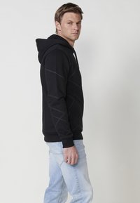 Hanorac negru cu un model geometric, având glugă cu șnur și manșete ribben. Asortat cu blugi bleu deschis.