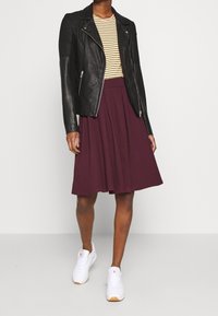 Chaqueta de motorista de cuero negro con hombros texturizados, camiseta de rayas de manga larga, falda en A color burdeos y zapatillas blancas con suelas de goma.