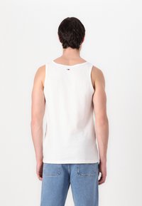 Hvid bomulds tanktop med en rund halsudskæring og brede ærmegab. Har et lille logo på ryggen. Kombineret med lyseblå jeans.