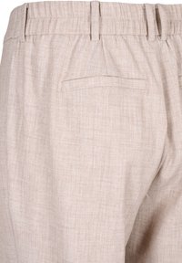 Pantalon beige en tissu texturé, avec une coupe décontractée, une ceinture élastique et une poche arrière unique.