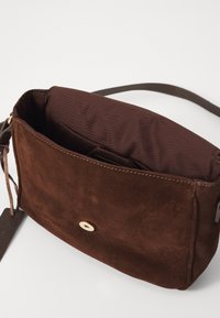 Brown suede crossbody bag with a smooth texture, gold accent button, and a spacious interior lined in dark fabric. Adjustable strap included.