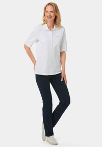 Weißes Kurzarm-Polohemd mit Kragen und dreiknöpfiger Blende, kombiniert mit dunkelblauen Jeans und hellen Sneakers.