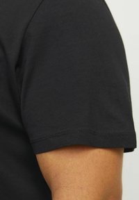 T-shirt noir à manches courtes en coton, avec une texture lisse et un col rond classique. Détails de couture le long de l'ourlet.