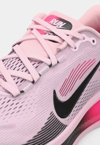 Baskets de course Nike en rose clair avec des accents noirs, dotées d'une tige en mesh, de lignes texturées et d'une semelle rose contrastante.